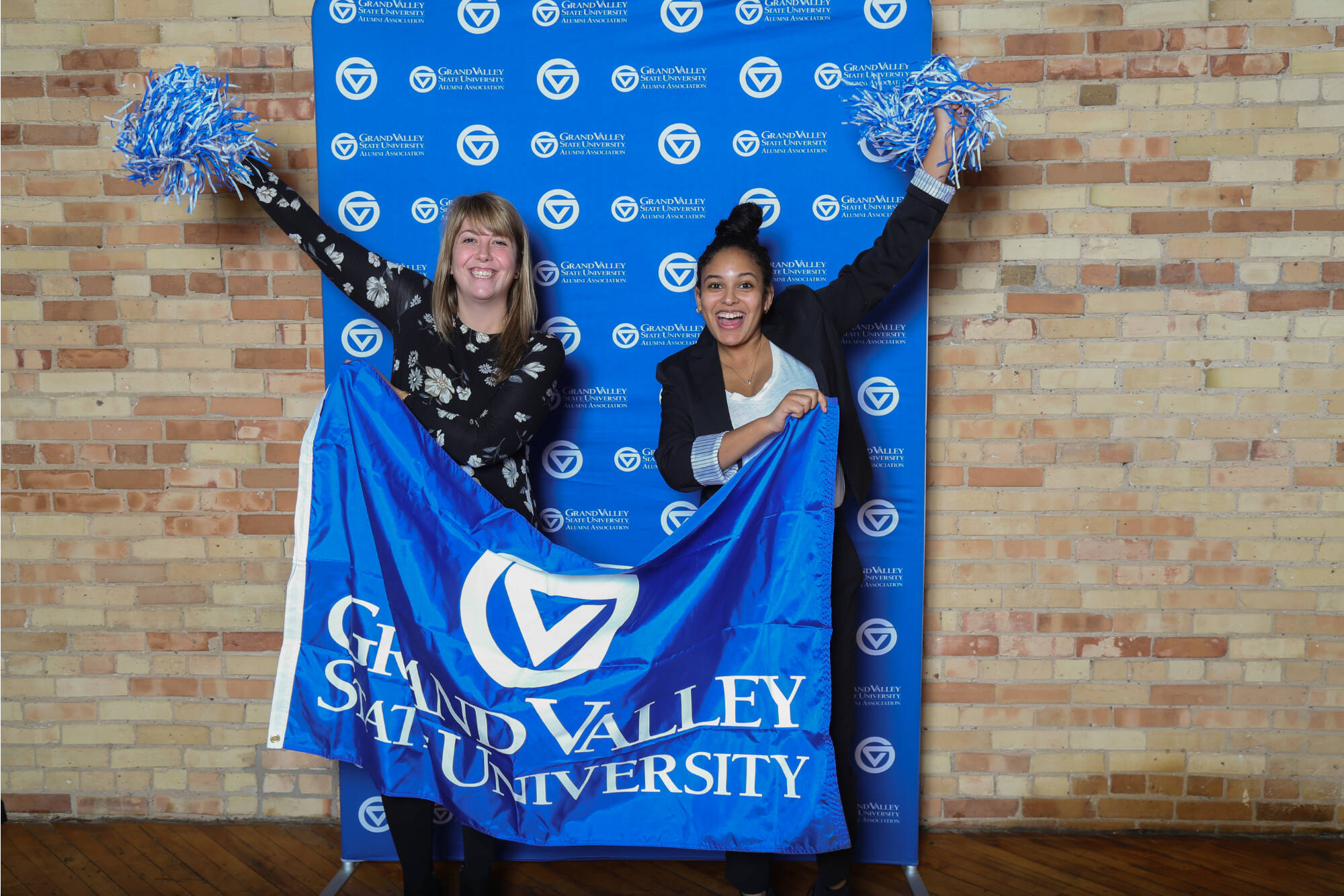 Two alumni women with GVSU banner and pompoms